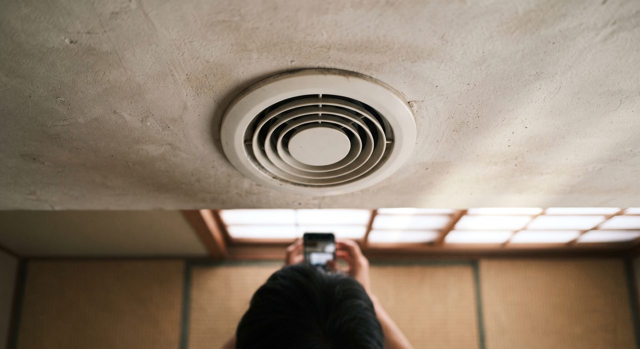 和室の天井にある丸い換気口(給気口)をスマートフォンで見上げて撮影しながら確認している様子